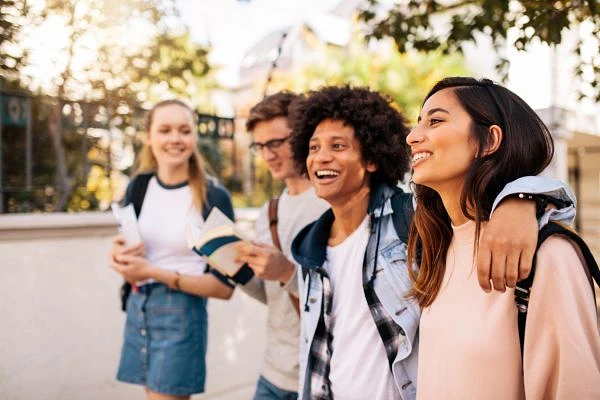 Four young friends are walking together outside, smiling and enjoying a sunny day.